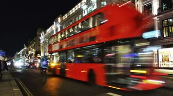 A red double-decker bus speeding through a busy city street at night