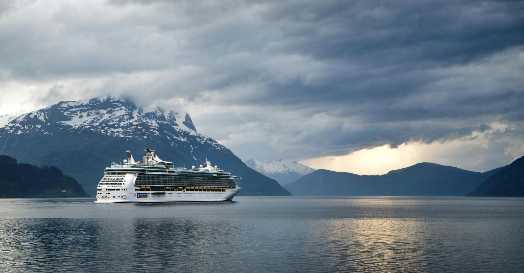 A cruise ship sailing against a backdrop of mountains under a cloudy sky