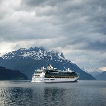 A cruise ship sailing against a backdrop of mountains under a cloudy sky