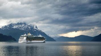 A cruise ship sailing against a backdrop of mountains under a cloudy sky
