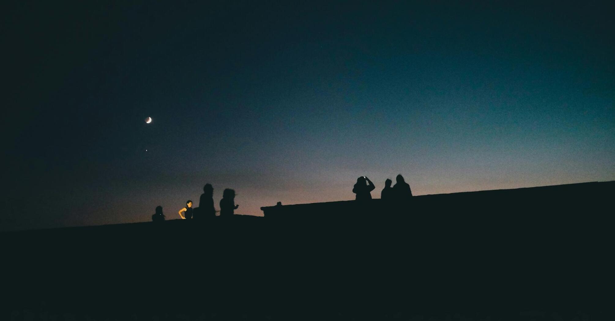 Silhouettes of people under a dark sky with a crescent moon and stars