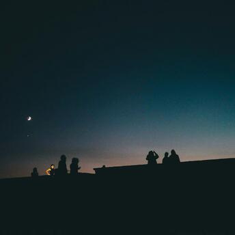 Silhouettes of people under a dark sky with a crescent moon and stars