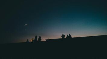 Silhouettes of people under a dark sky with a crescent moon and stars