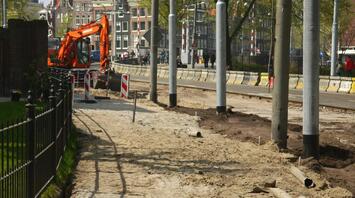 Heavy equipment operating at a road construction site, with barriers and excavated paths