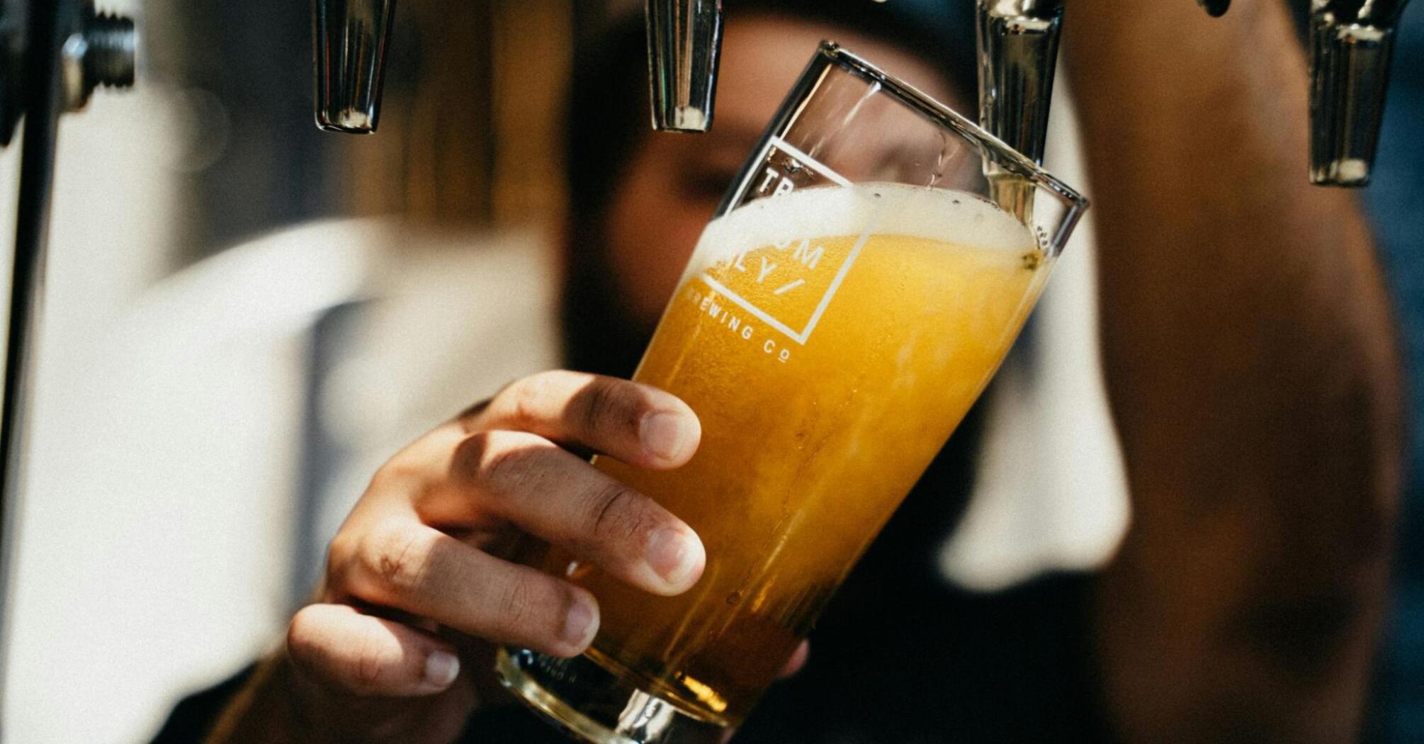 A person pours a glass of draft beer from a tap