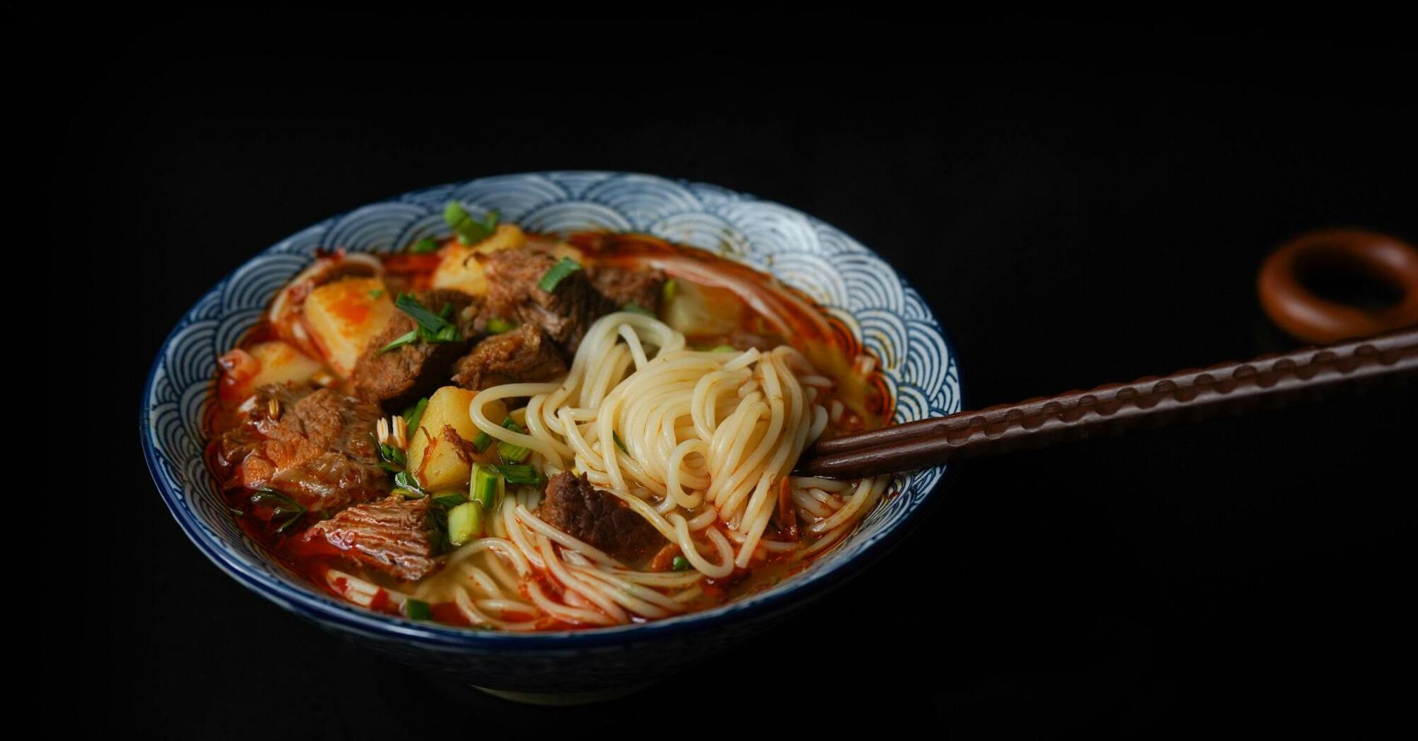 Bowl of ramen with noodles, beef, and vegetables served with chopsticks