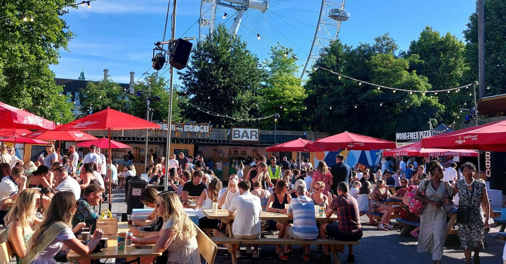 Outdoor dining area with people enjoying food and drinks near the London Eye