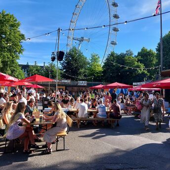 Outdoor dining area with people enjoying food and drinks near the London Eye