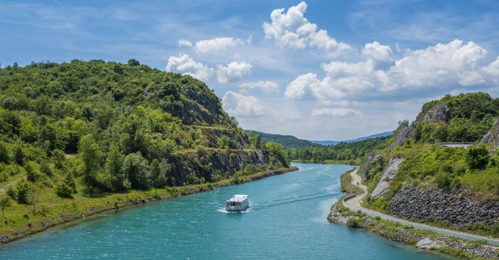 A serene riverboat cruising along a winding river surrounded by green hills under a bright blue sky