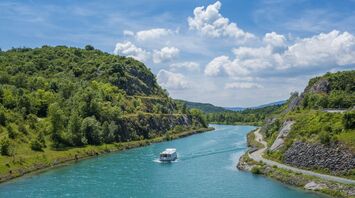 A serene riverboat cruising along a winding river surrounded by green hills under a bright blue sky