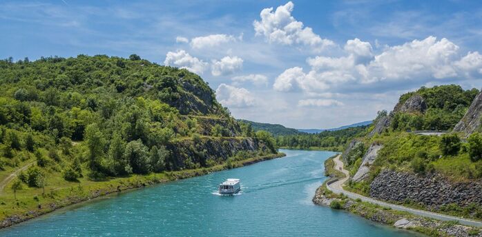 A serene riverboat cruising along a winding river surrounded by green hills under a bright blue sky