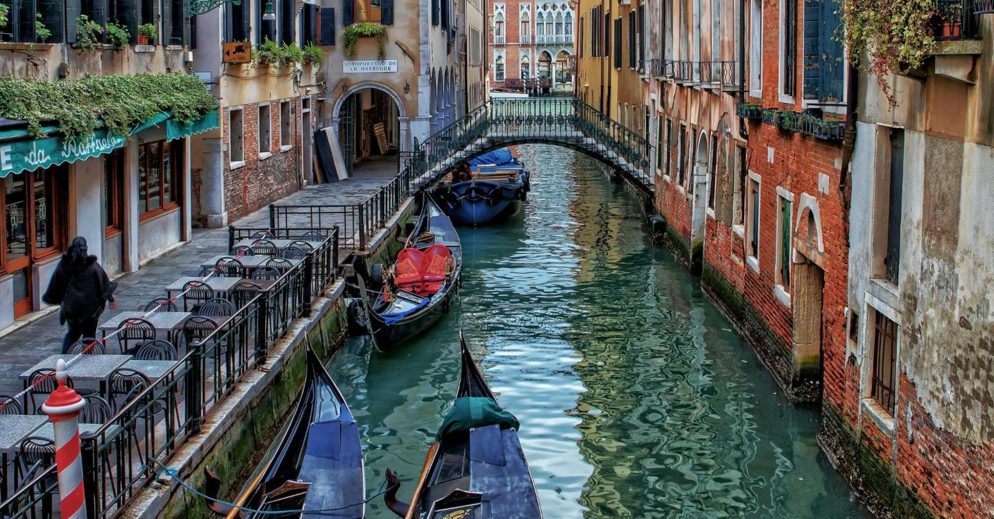 Quiet canal with gondolas and an empty café terrace in Venice