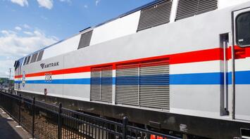 A modern Amtrak train with a red, white, and blue stripe design parked at a station under a clear sky