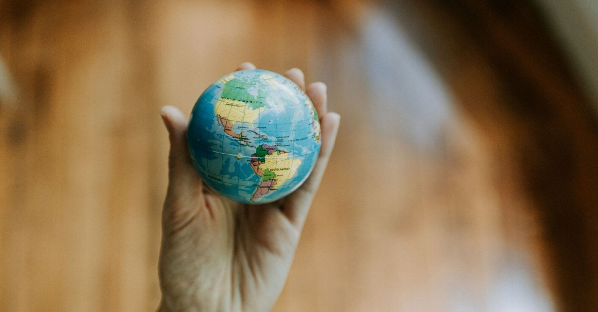 A hand holding a small globe focused on the Americas, symbolizing travel and exploration