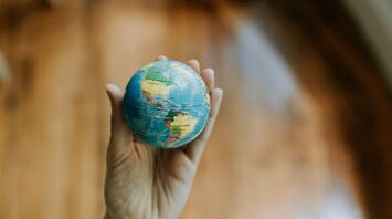 A hand holding a small globe focused on the Americas, symbolizing travel and exploration
