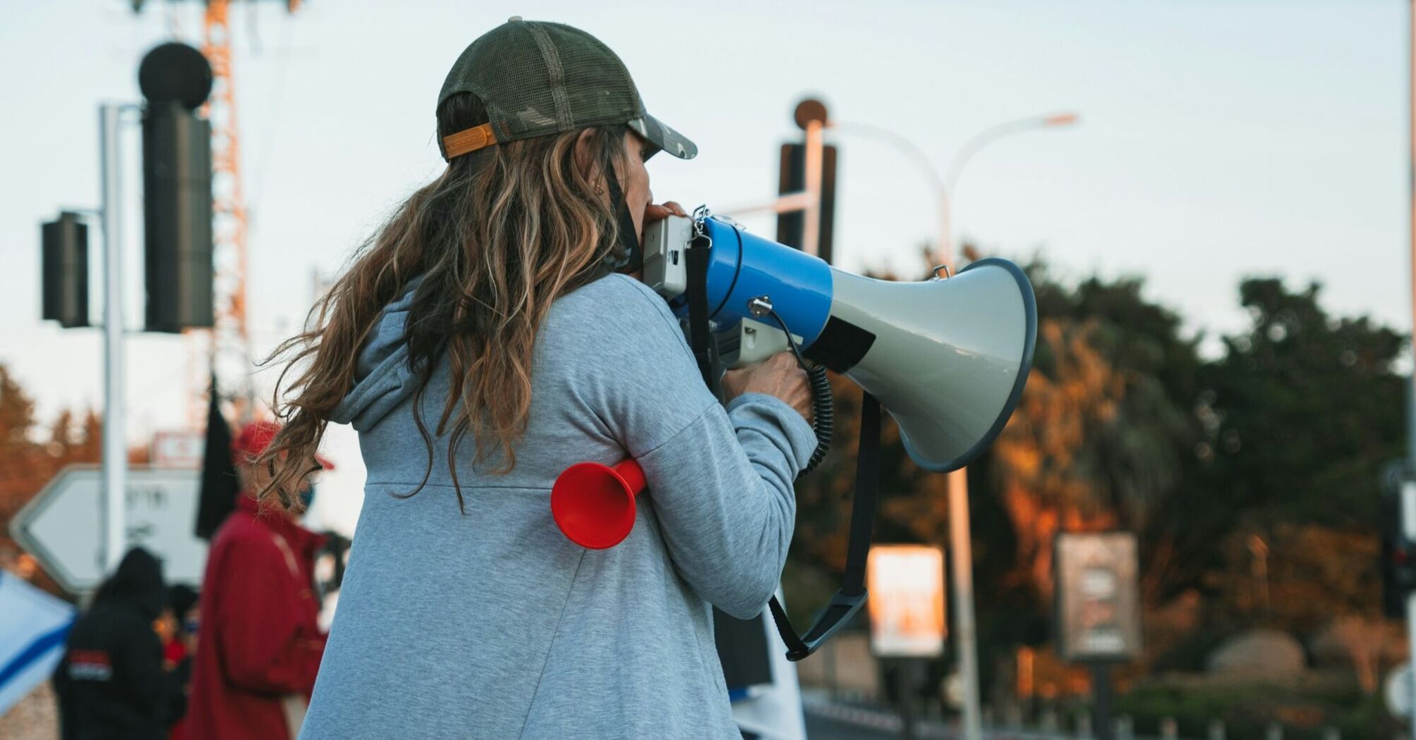 A person in a gray hoodie using a megaphone during a public demonstration