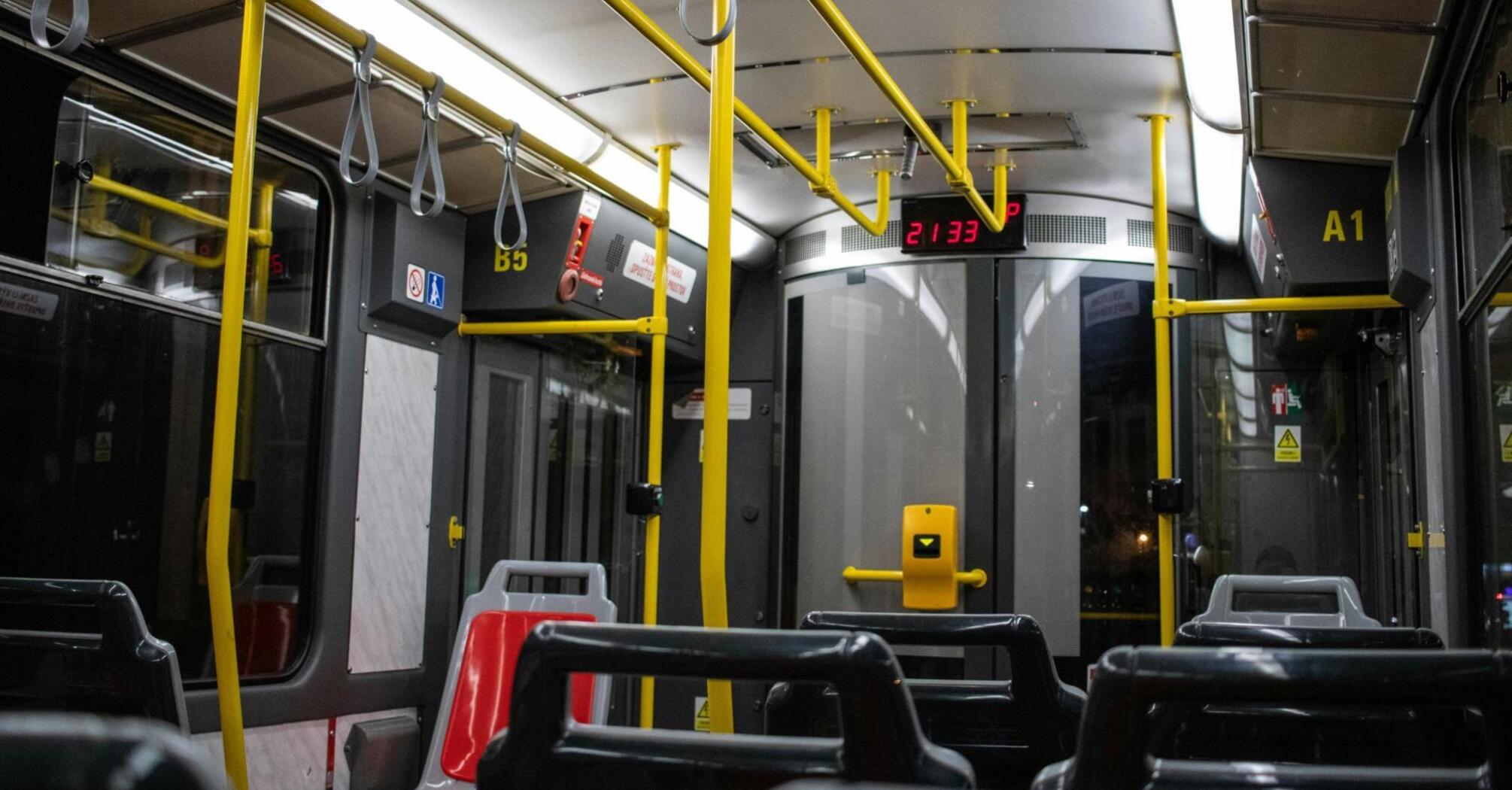 An empty public bus interior with bright yellow handrails, captured at night