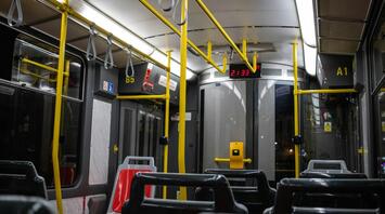 An empty public bus interior with bright yellow handrails, captured at night
