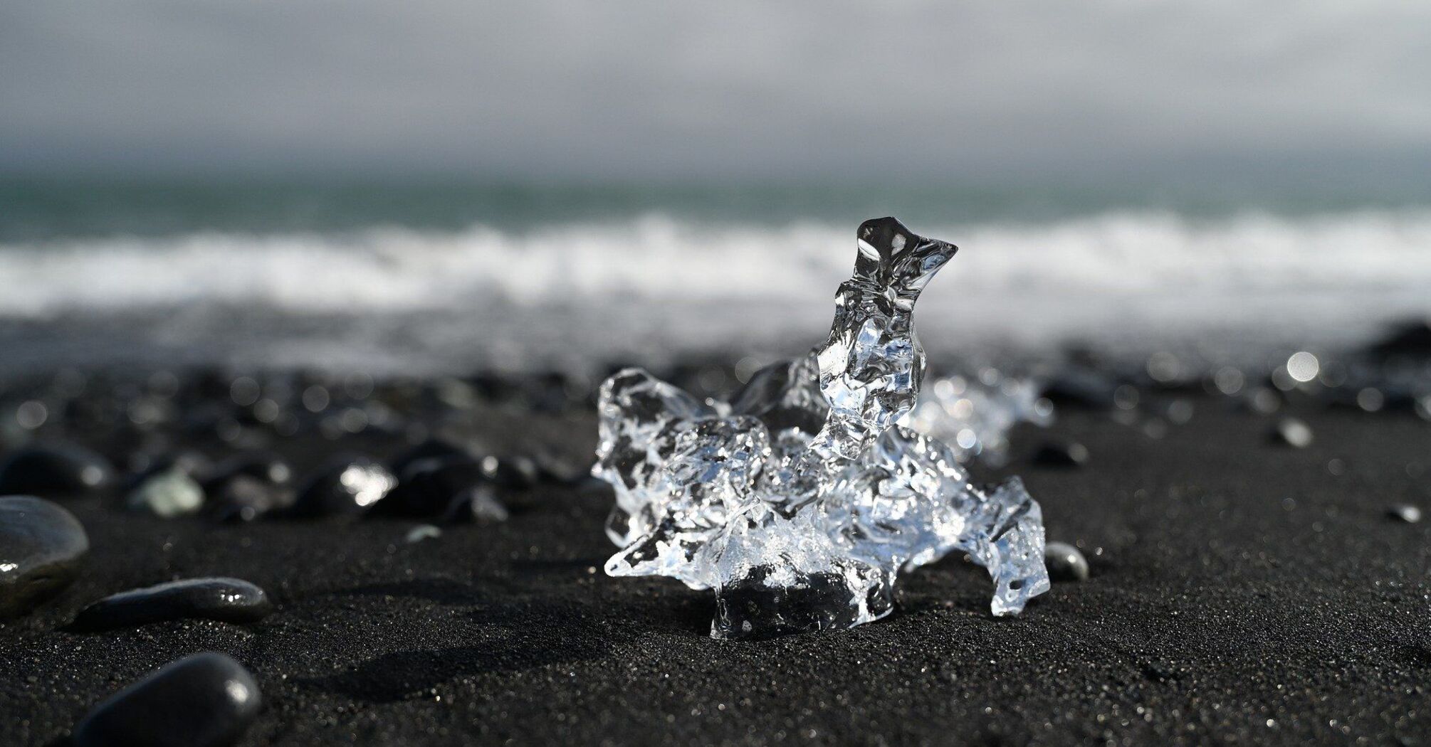 Piece of ice on a black sand beach with ocean waves in the background