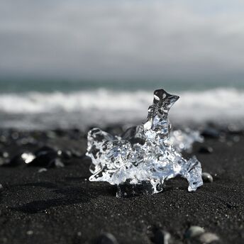Piece of ice on a black sand beach with ocean waves in the background