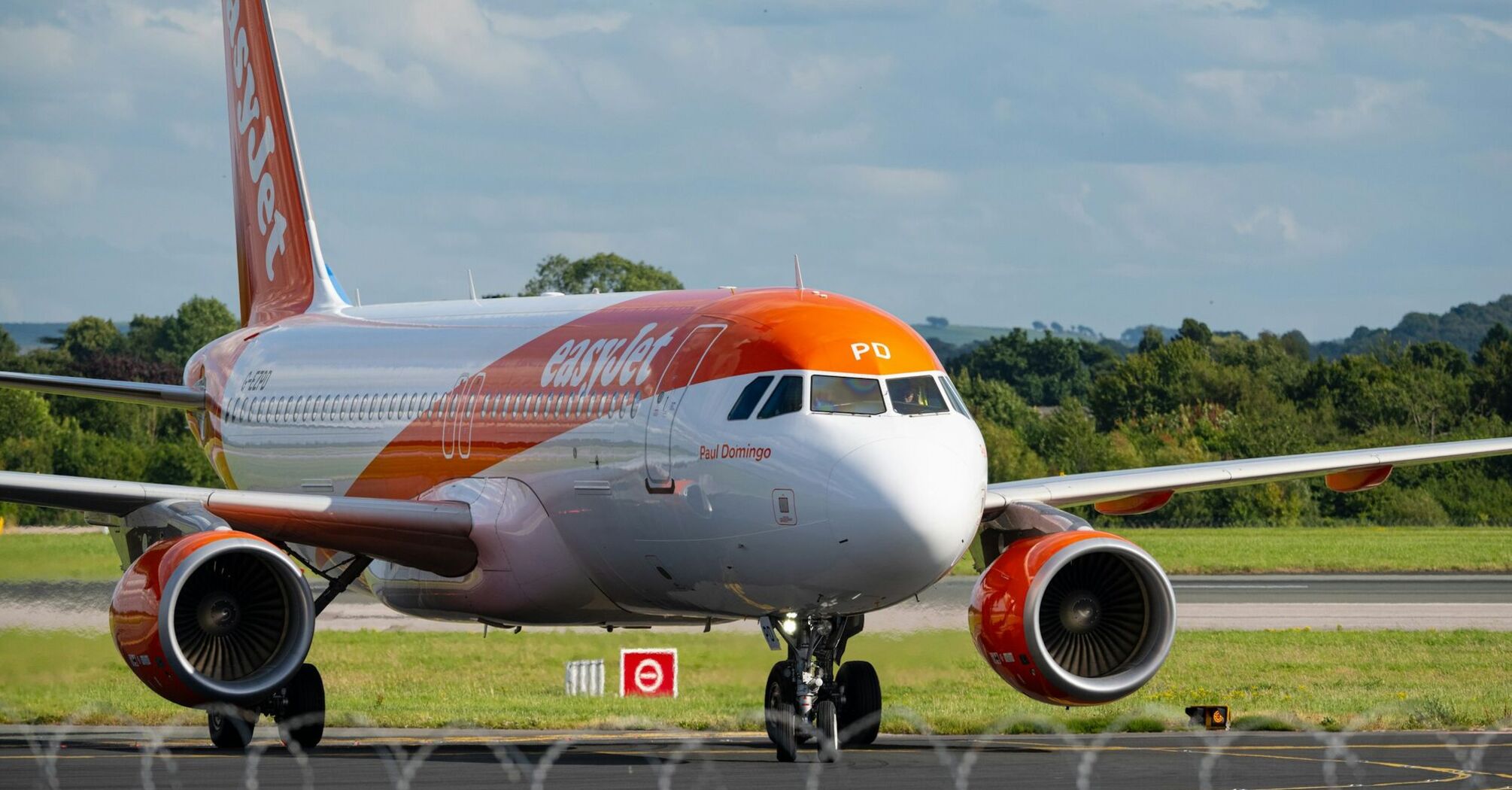 An easyJet aircraft on the runway preparing for takeoff at an airport, surrounded by green landscape and a partly cloudy sky