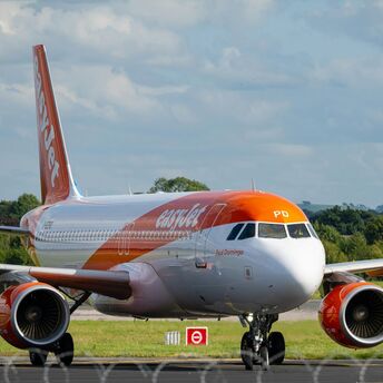 An easyJet aircraft on the runway preparing for takeoff at an airport, surrounded by green landscape and a partly cloudy sky