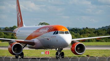 An easyJet aircraft on the runway preparing for takeoff at an airport, surrounded by green landscape and a partly cloudy sky