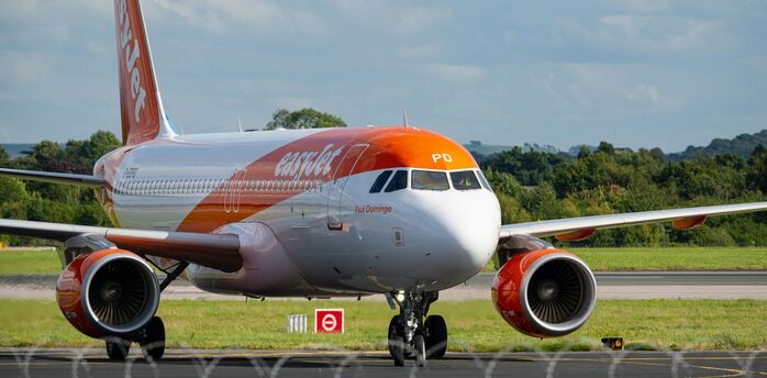 An easyJet aircraft on the runway preparing for takeoff at an airport, surrounded by green landscape and a partly cloudy sky