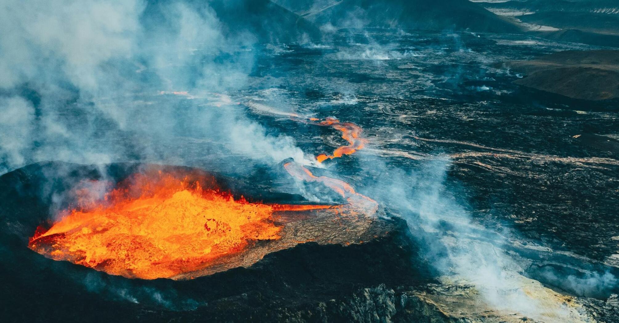 Aerial view of an active volcanic eruption with lava flowing across rugged terrain in Iceland