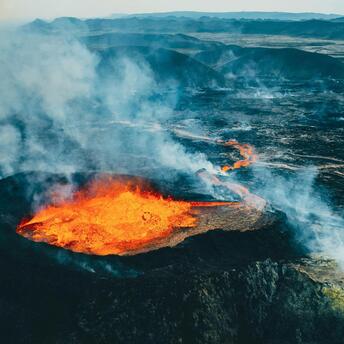 Aerial view of an active volcanic eruption with lava flowing across rugged terrain in Iceland