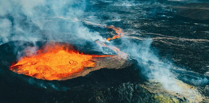 Aerial view of an active volcanic eruption with lava flowing across rugged terrain in Iceland