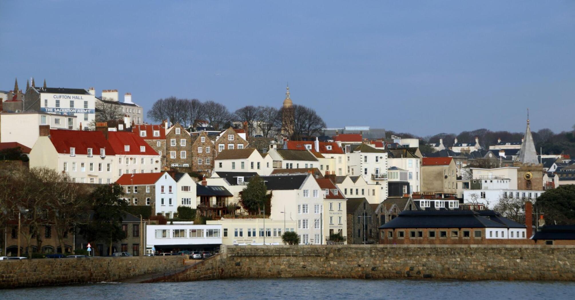 A view of Saint Peter Port in Guernsey with a mix of historic stone buildings and newer structures along the waterfront