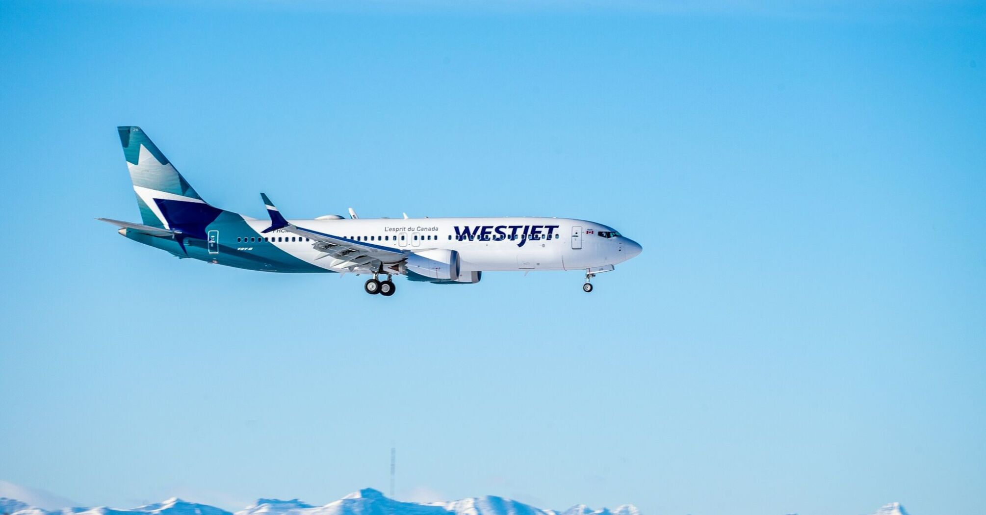 A WestJet Boeing 737 aircraft in flight against a clear blue sky with mountains in the background