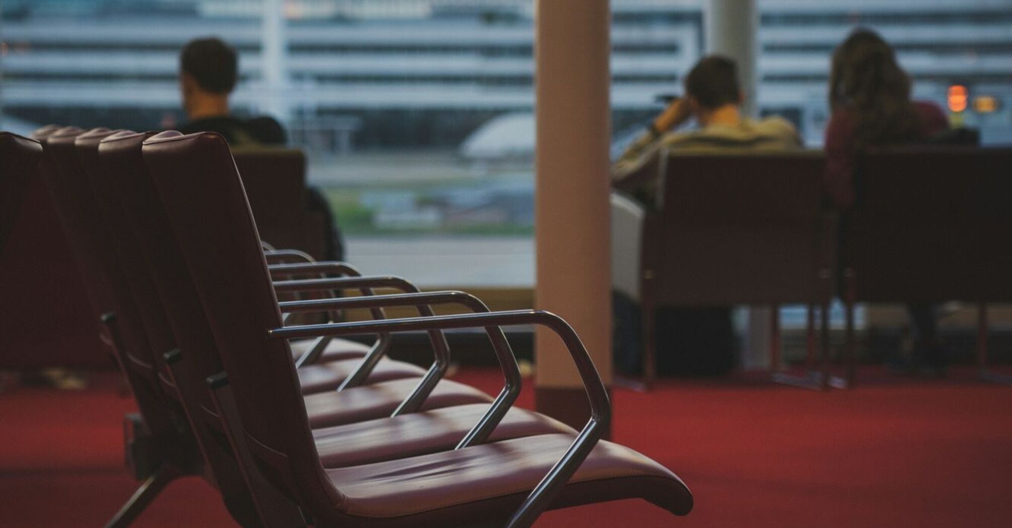 Empty airport seating area with a view of the tarmac, passengers waiting in the background