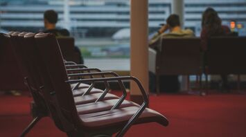 Empty airport seating area with a view of the tarmac, passengers waiting in the background