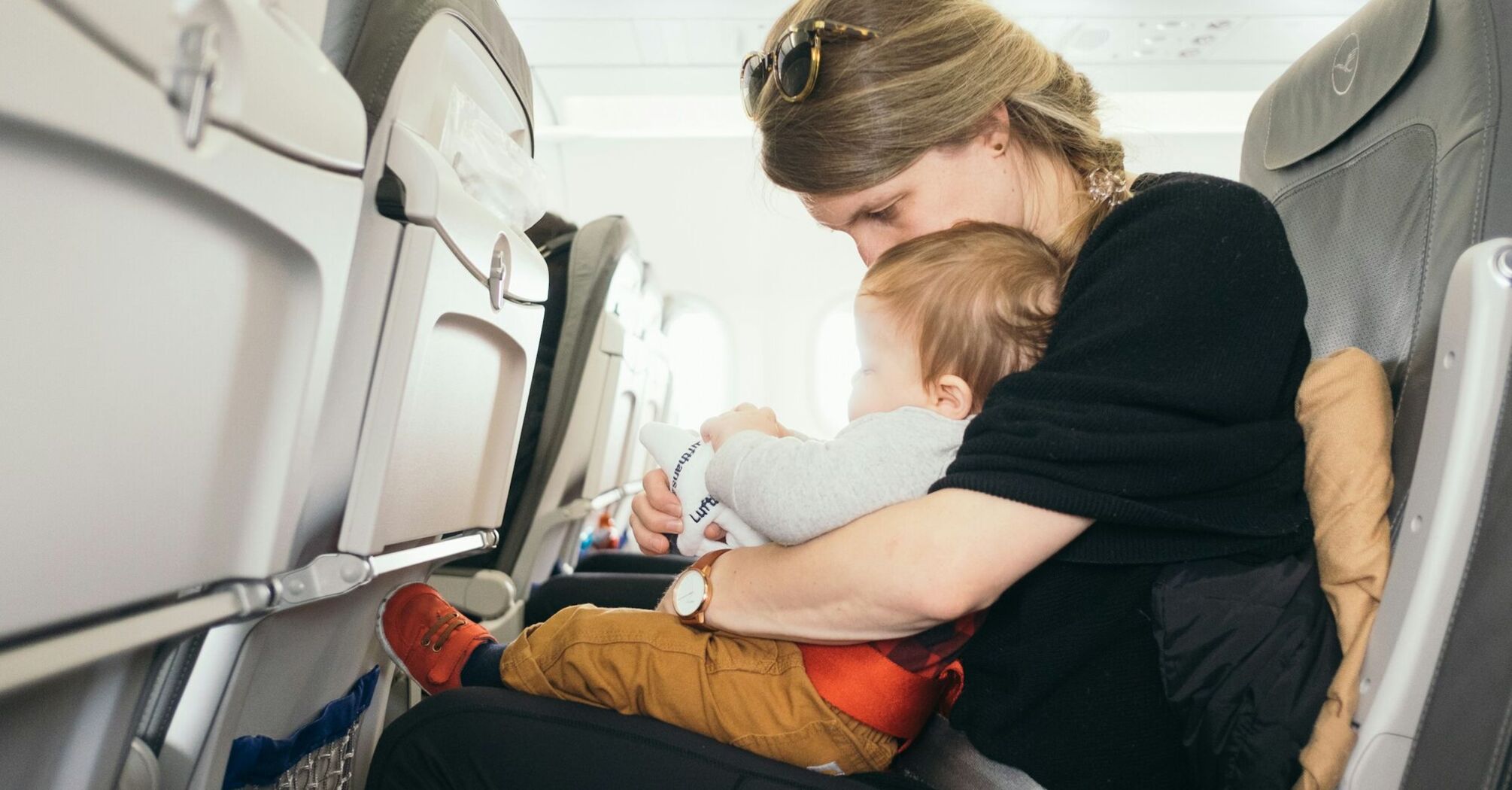 A mother holding her baby on her lap while seated on an airplane