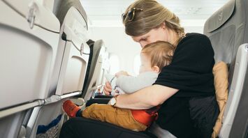 A mother holding her baby on her lap while seated on an airplane
