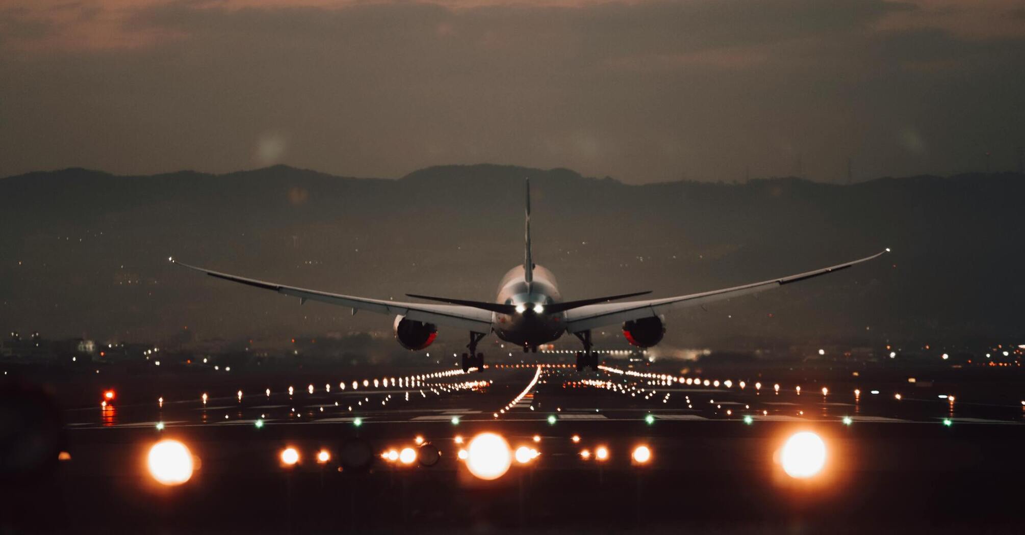 Airplane taking off at dusk with runway lights illuminated