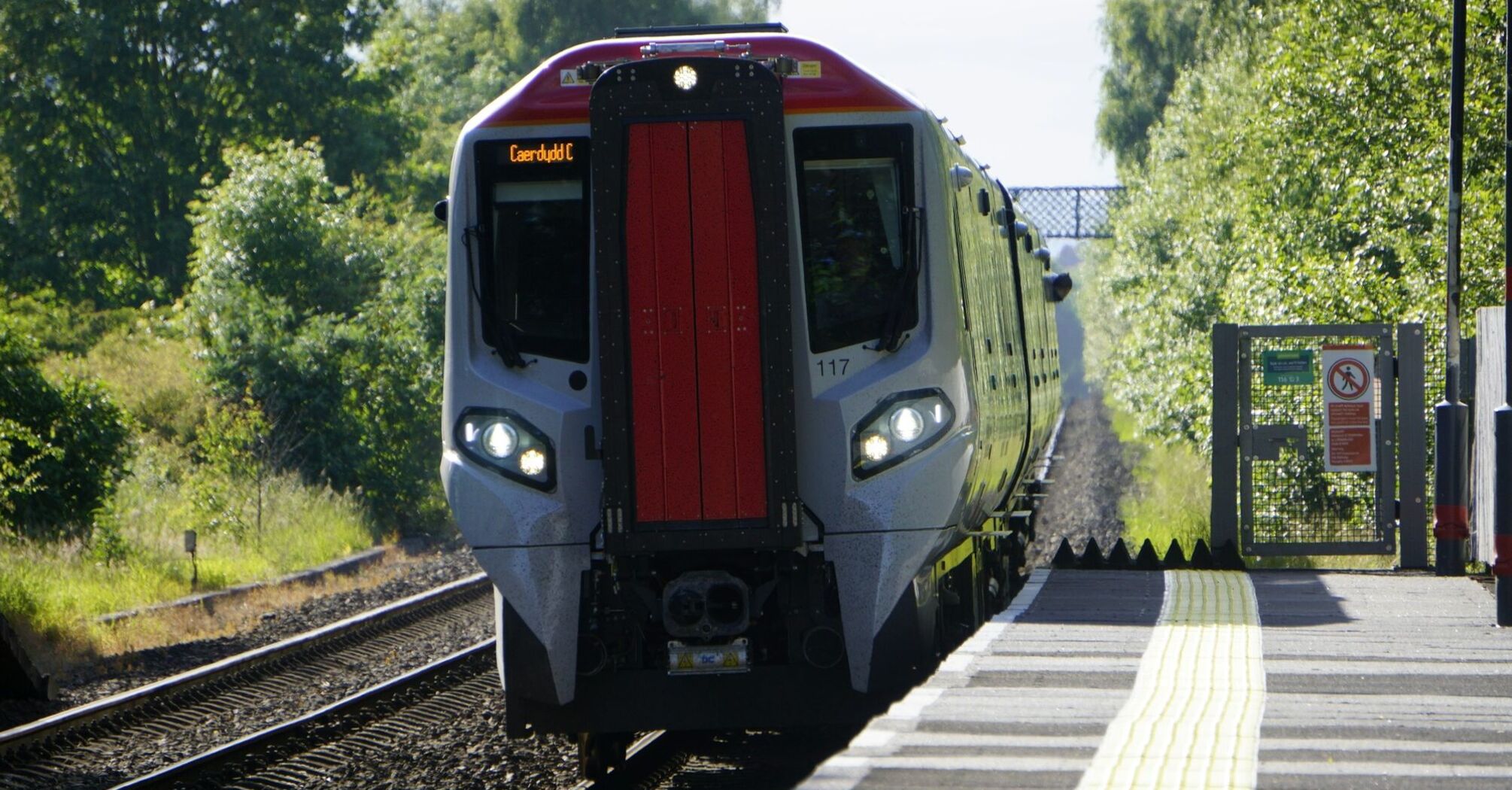 A modern electric train arriving at a station on a sunny day with trees in the background