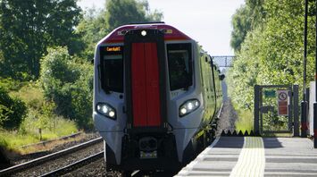 A modern electric train arriving at a station on a sunny day with trees in the background