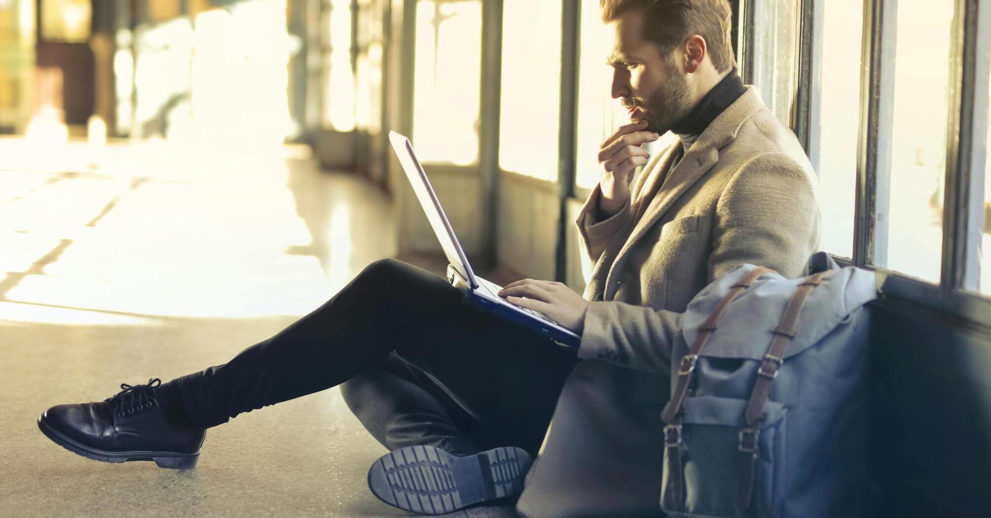 Man sitting on the floor with a laptop and backpack in an airport