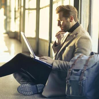 Man sitting on the floor with a laptop and backpack in an airport