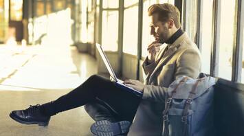 Man sitting on the floor with a laptop and backpack in an airport