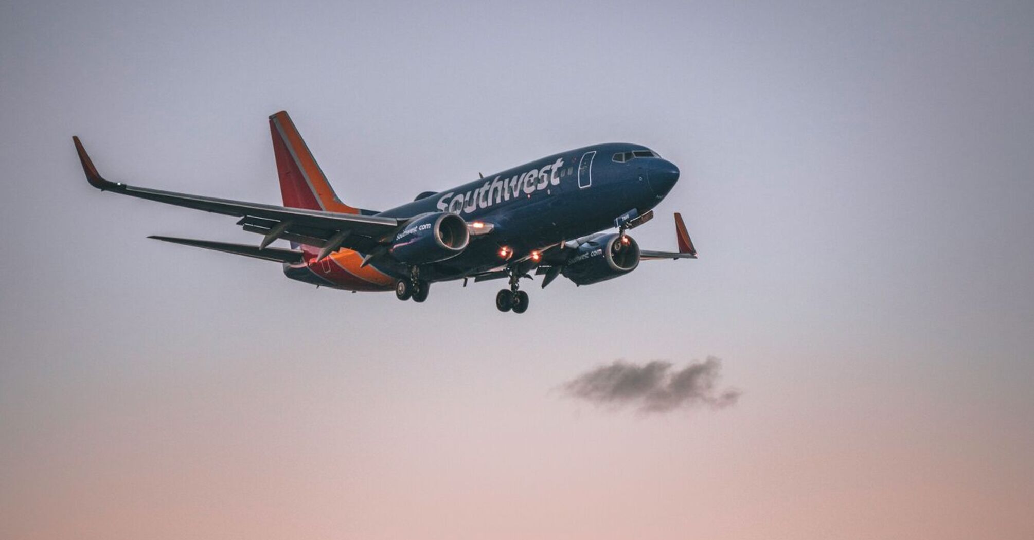 A Southwest Airlines plane approaching landing at sunset, with palm trees silhouetted in the foreground