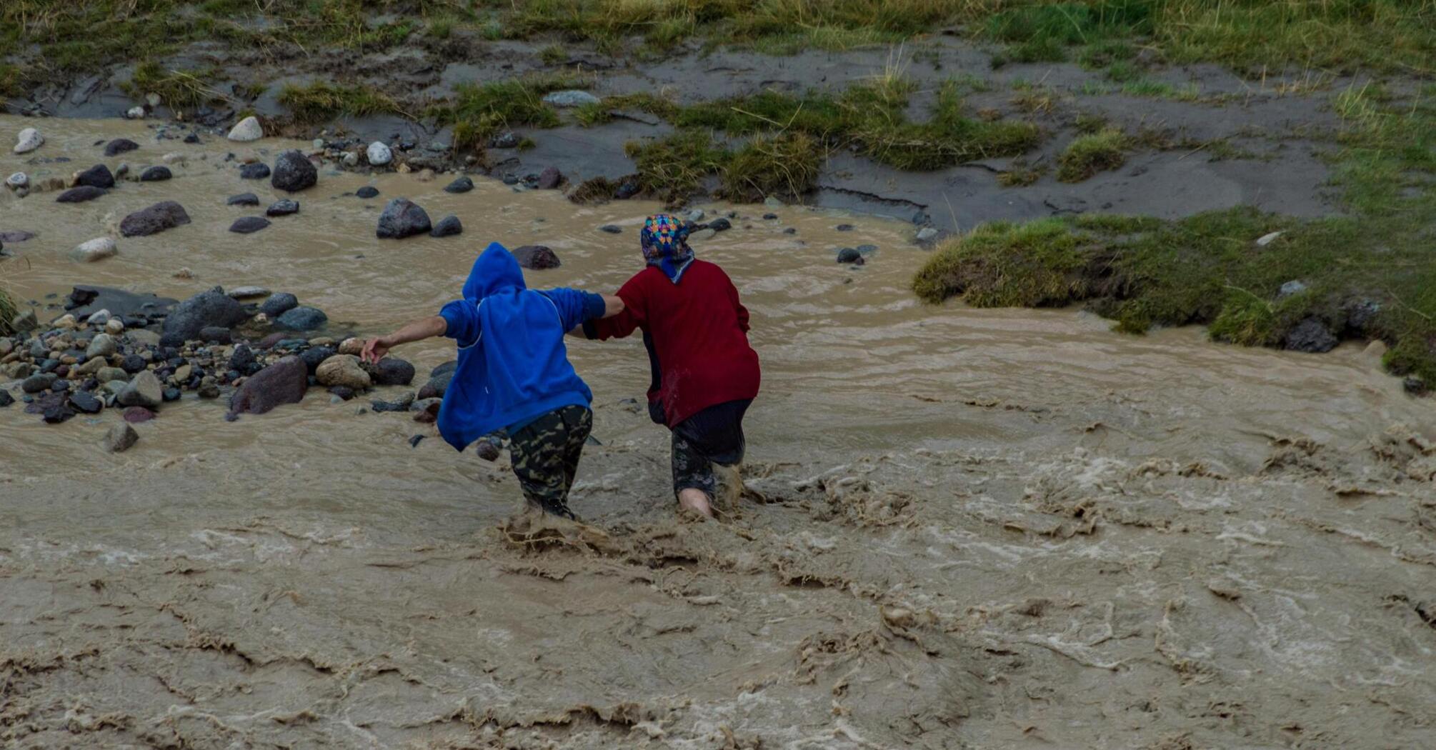 Two people helping each other cross a flooded area