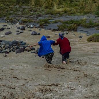 Two people helping each other cross a flooded area