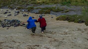 Two people helping each other cross a flooded area