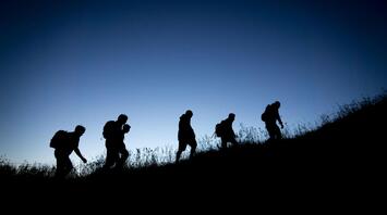 Silhouetted group of hikers walking up a hill at dusk, representing adventure and exploration