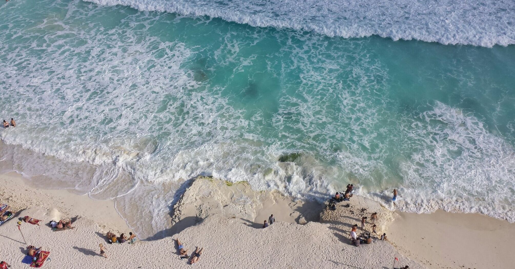 Tourists relaxing on a white sand beach in Cancun with waves crashing on the shore