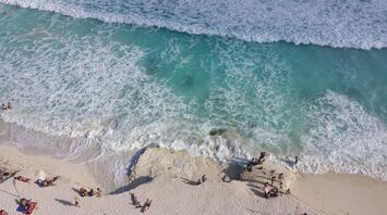 Tourists relaxing on a white sand beach in Cancun with waves crashing on the shore
